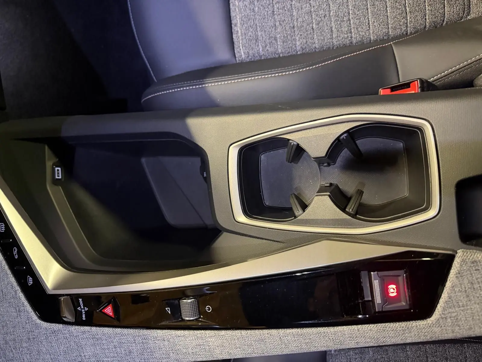 Gros plan sur la console centrale grise du Peugeot 3008 1.2 Hybrid 136 Allure avec porte-gobelets et bouton de frein à main électronique.