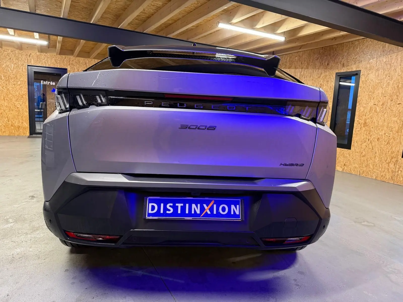Vue arrière d'un Peugeot 3008 gris hybride 2025 avec signature lumineuse distinctive et toit noir dans un garage.