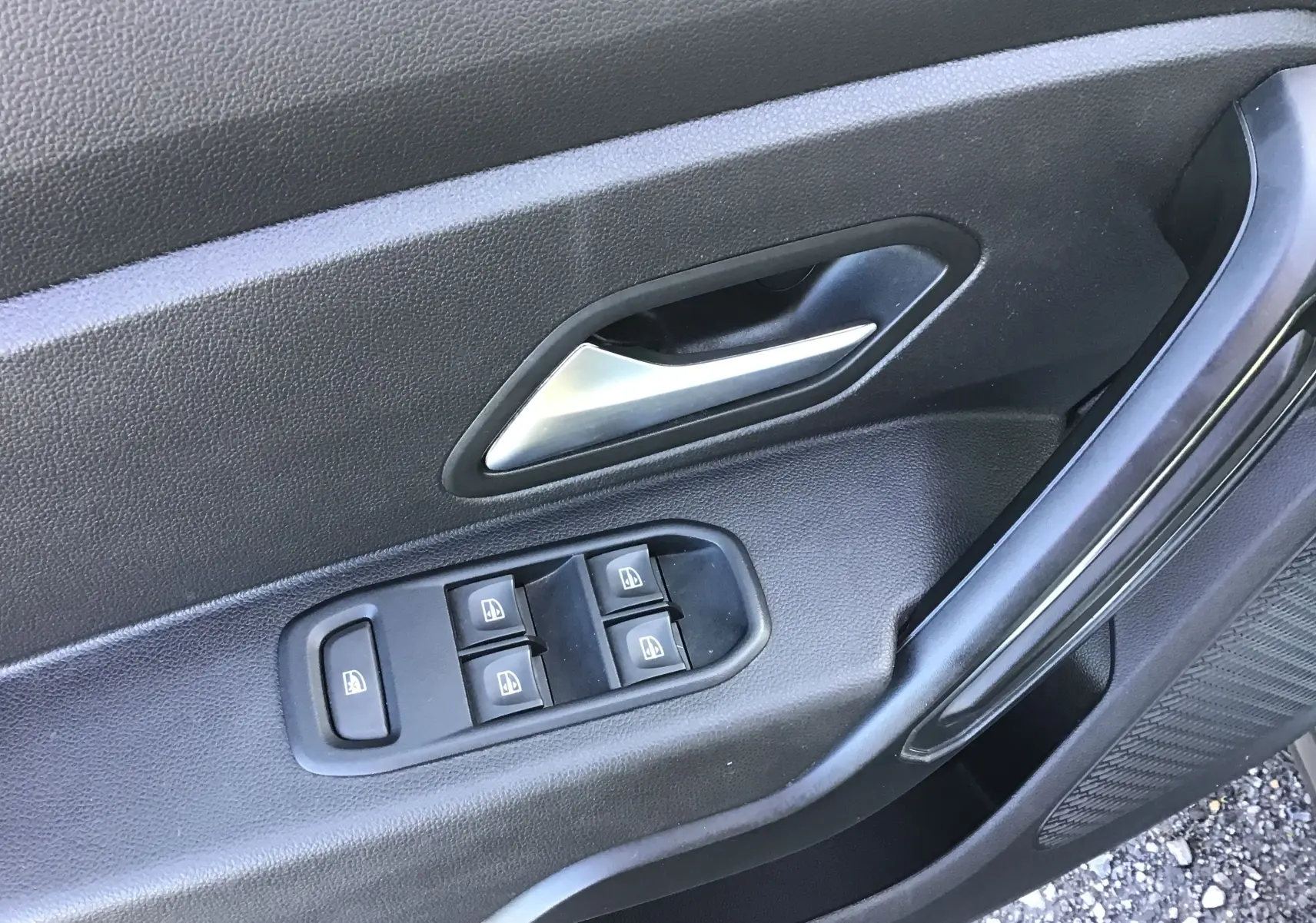 Gros plan sur la porte avant gauche noire du Dacia Duster blanc 2021, montrant les commandes des vitres électriques et la poignée intérieure.