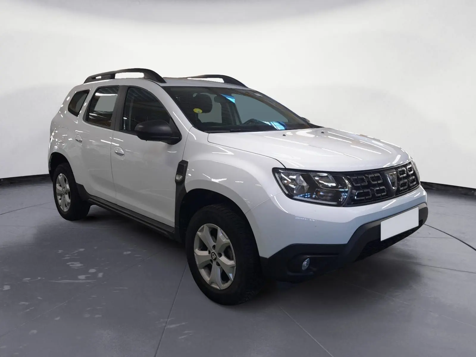 Profil côté gauche d'un Dacia Duster blanc 2021, version 4x2, avec jantes alliage et toit noir sous un abri extérieur.