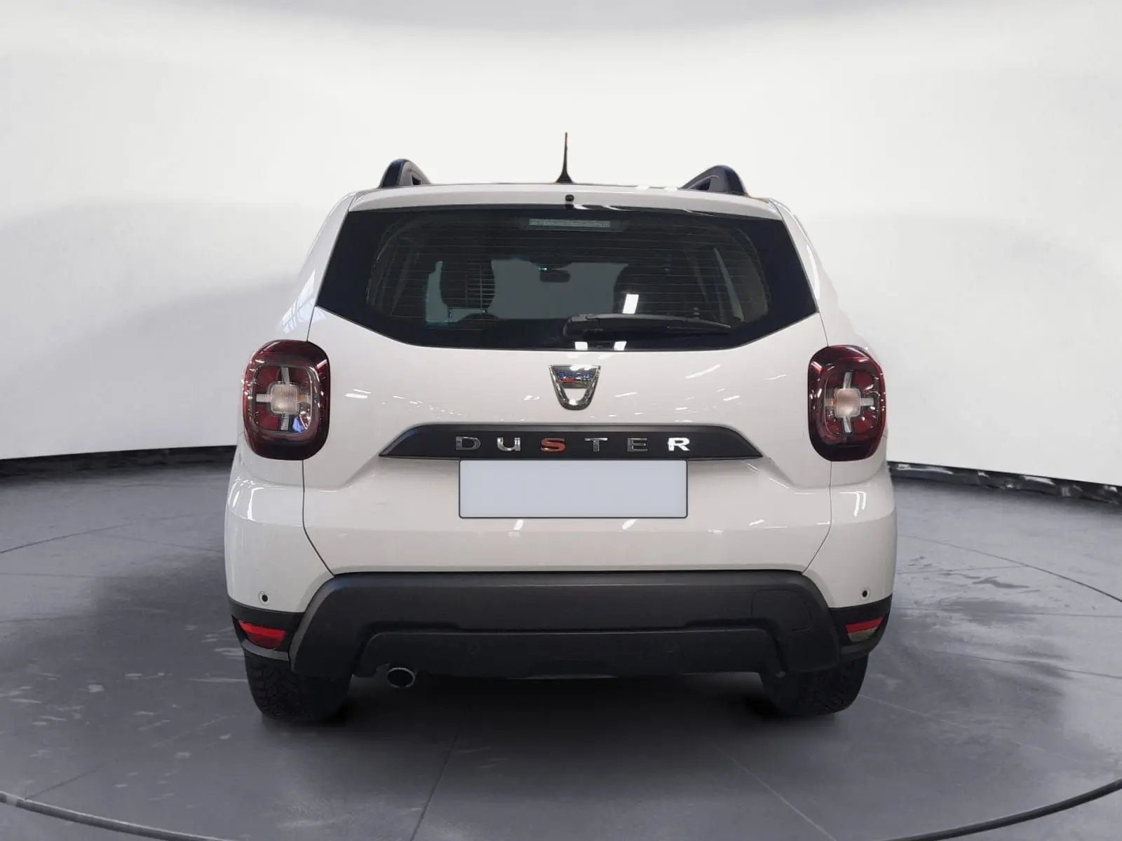 Vue 3/4 arrière droite d'un Dacia Duster blanc 2021 avec jantes alliage et grille de séparation visible à l'arrière.