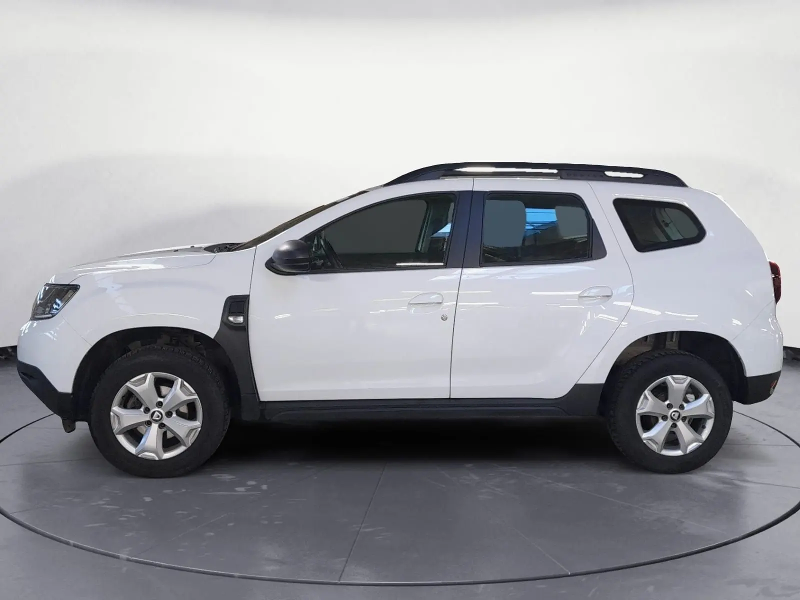 Vue arrière du coffre ouvert d'un Dacia Duster blanc 2021 avec grille de séparation et revêtement plastique noir.