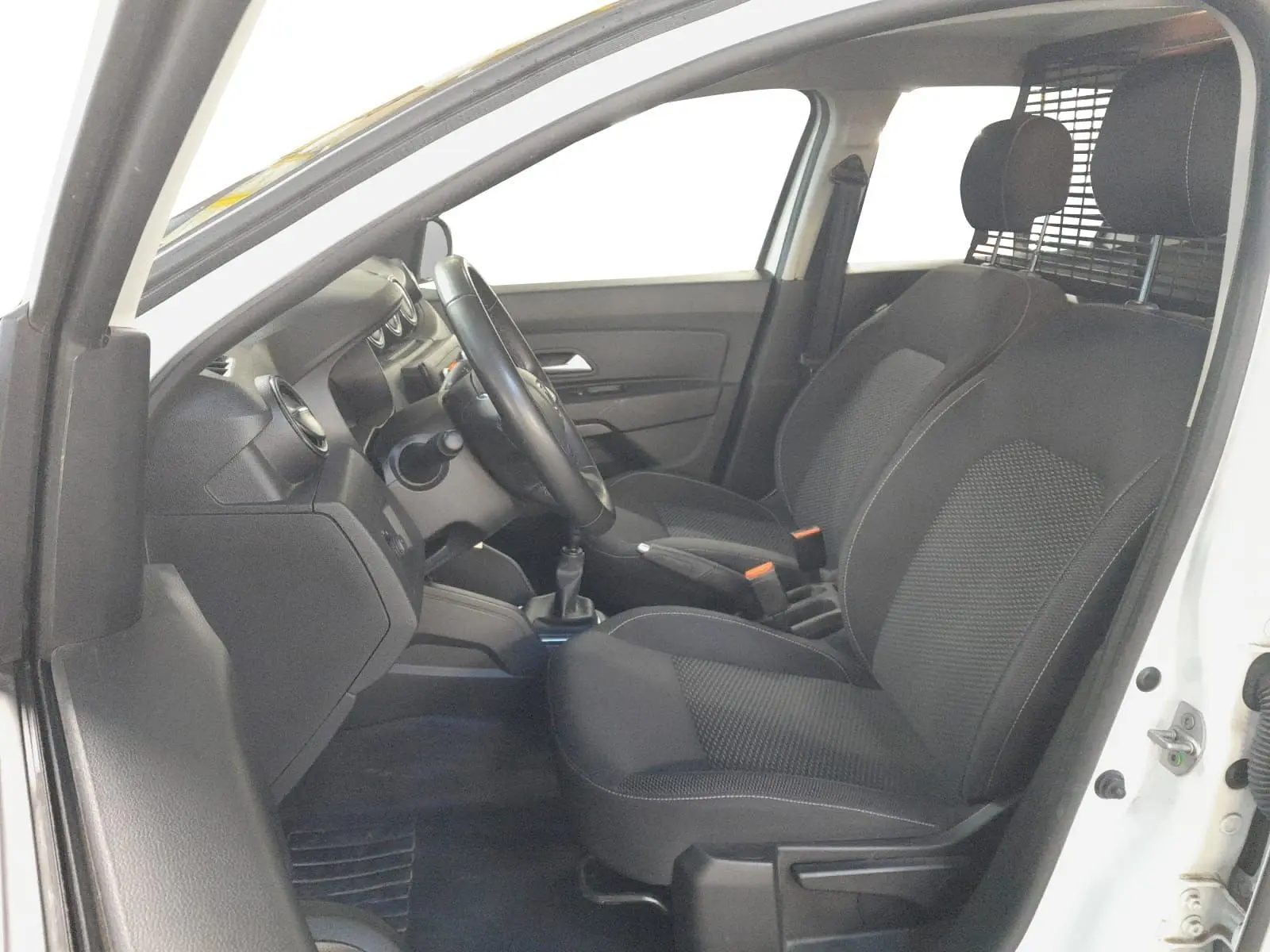 Vue intérieure côté conducteur du Dacia Duster blanc 2021, sièges noirs avec grille de séparation visible derrière.