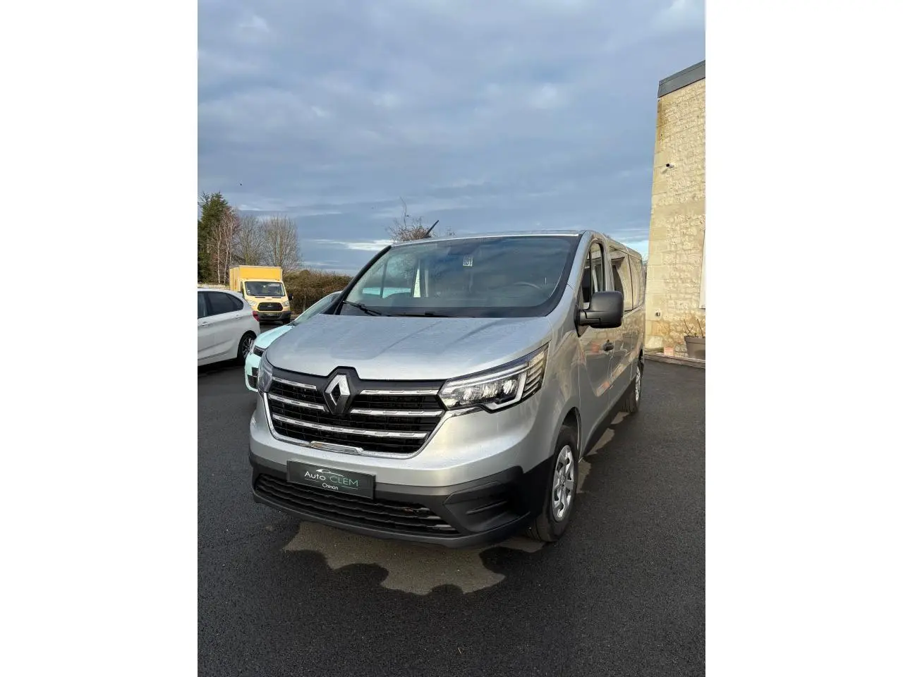 Renault Trafic Fourgon gris clair vu de face droite, avec calandre noire et phares LED distinctifs.