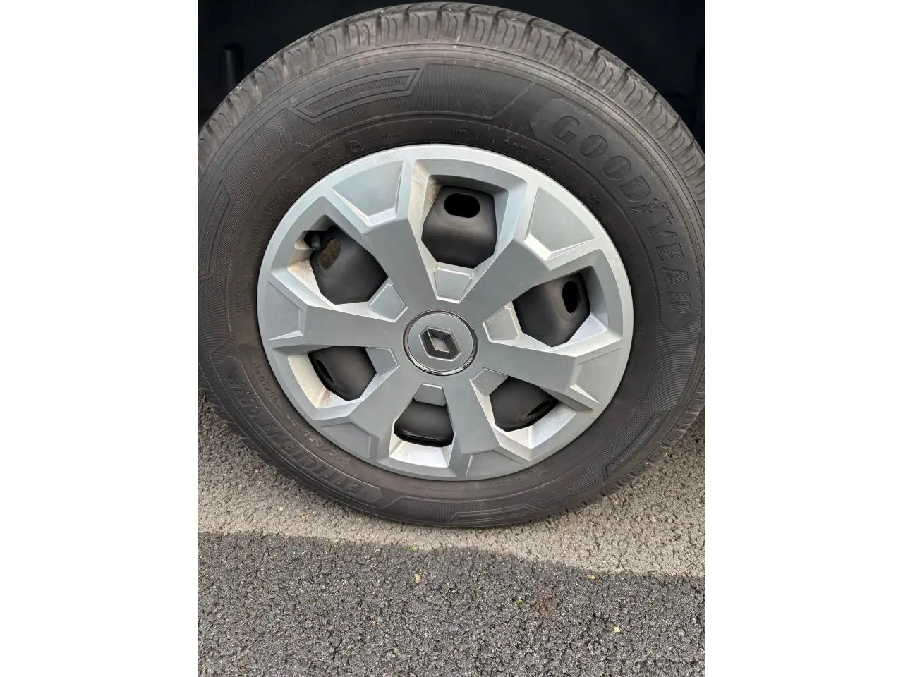 Gros plan sur la roue avec enjoliveur gris clair et logo Renault au centre, pneu Goodyear visible sur sol asphalté.