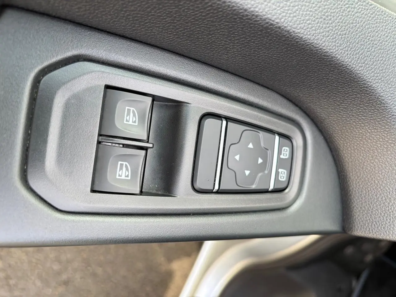 Gros plan sur les commandes de réglage des vitres et des rétroviseurs côté conducteur du Renault Trafic Fourgon gris clair.