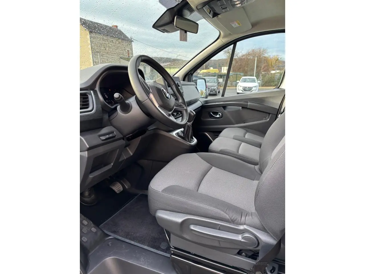 Vue intérieure côté conducteur du Renault Trafic Fourgon 2022, sièges gris et volant multifonctions visible.