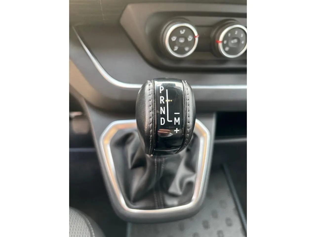 Gros plan sur le levier de vitesses automatique noir avec coutures, tableau de bord gris foncé en arrière-plan.