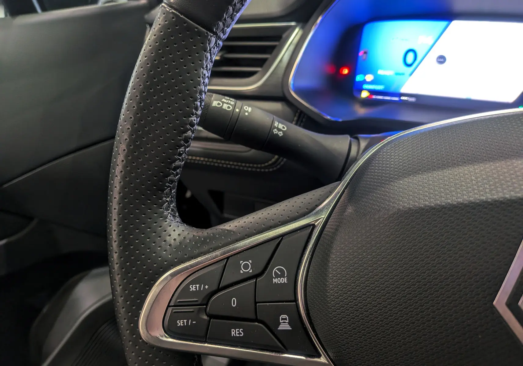 Gros plan sur le volant perforé noir du Renault Symbioz 2025 avec commandes multifonctions et tableau de bord numérique bleu.