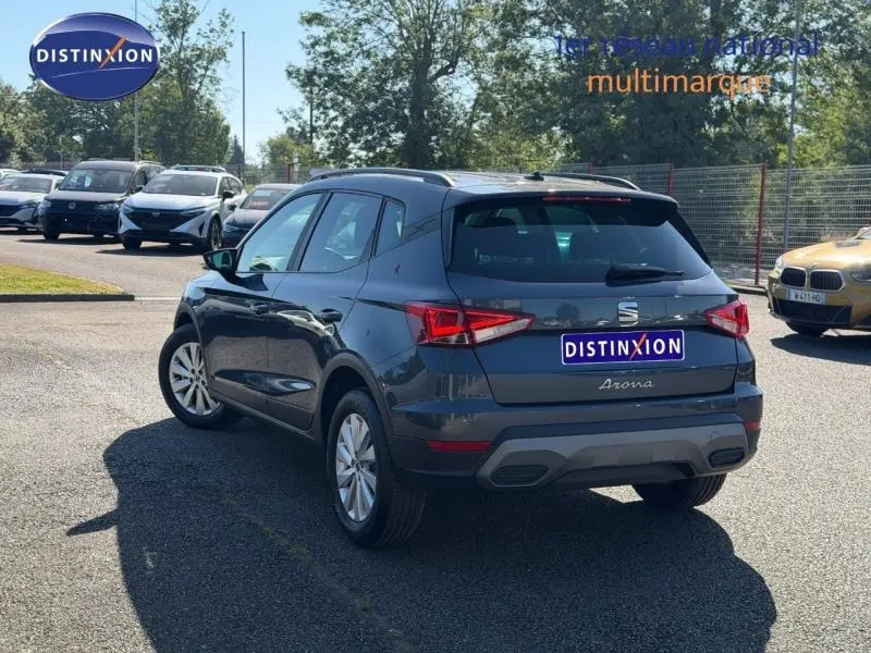 Vue 3/4 arrière droite d'un SEAT Arona gris magnétique avec toit noir, en extérieur sur parking lumineux.