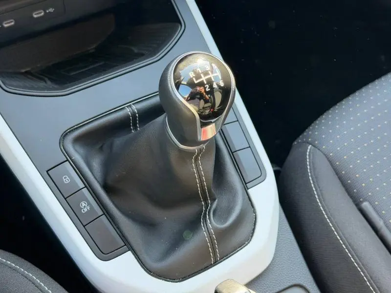 Gros plan sur le levier de vitesses manuel en cuir noir avec coutures blanches, intérieur tissu gris de la SEAT Arona 2025.