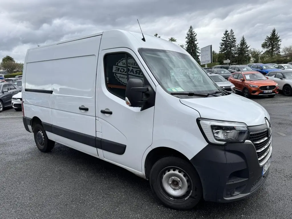 Renault Master blanc vu de 3/4 avant droit avec pare-chocs noir et roues tôlées sur parking sous ciel nuageux.