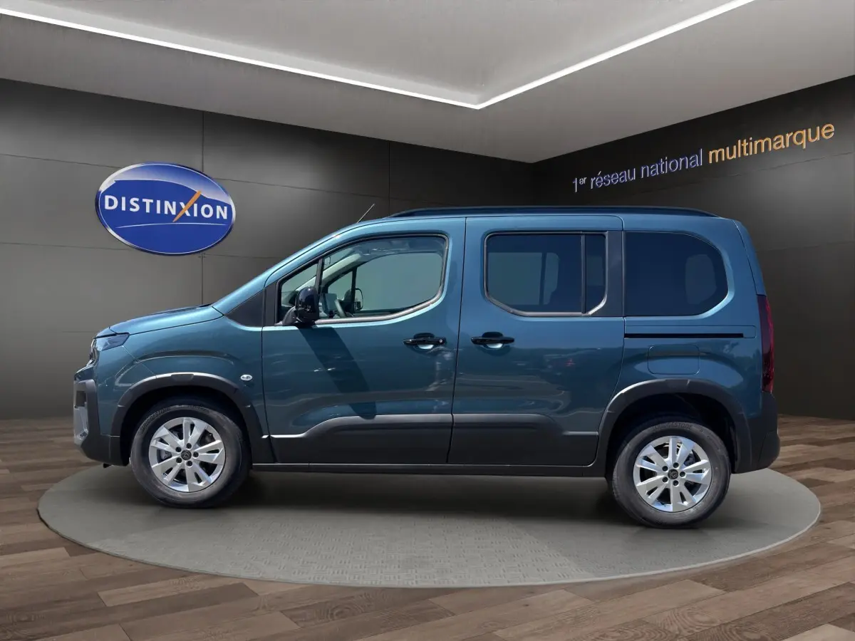 Vue de profil côté gauche du Peugeot Rifter bleu 2026 dans un showroom avec jantes argentées et portes coulissantes.