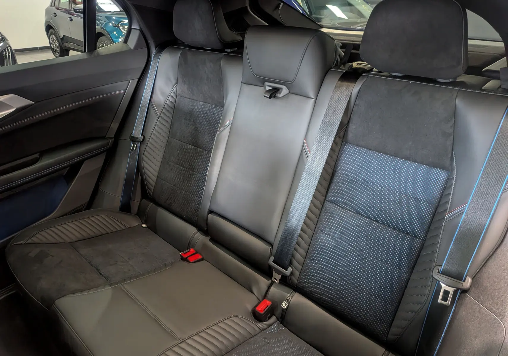 Vue intérieure sur la banquette arrière en cuir noir et alcantara avec surpiqûres rouges et ceintures de sécurité bleues.