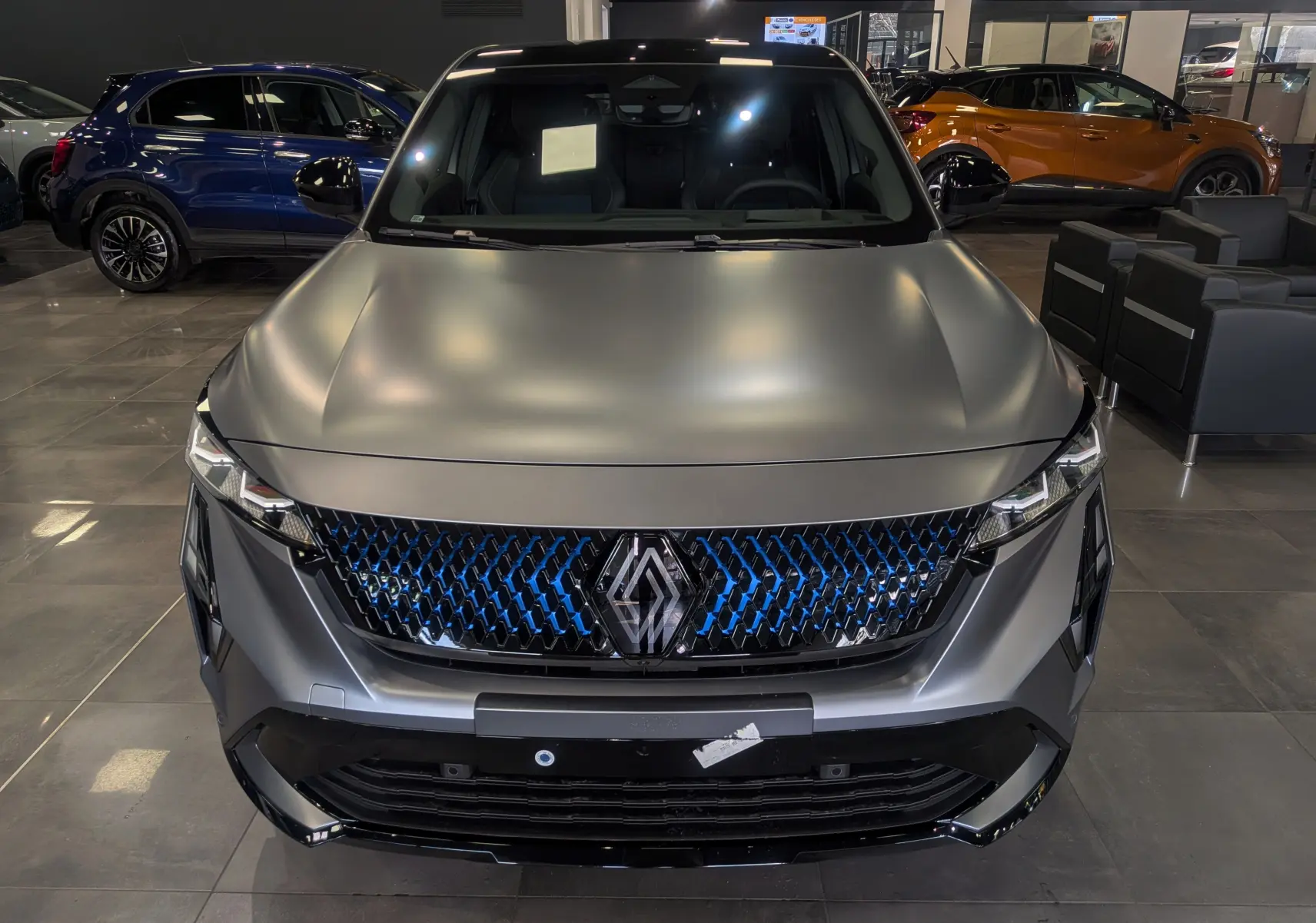 Vue avant rapprochée du Renault Rafale E-TECH gris schiste satin, avec calandre noire et détails bleus lumineux.