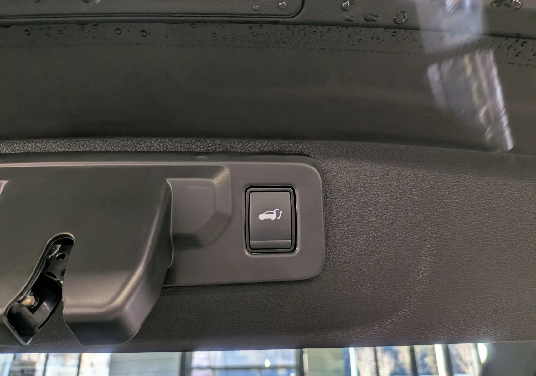 Bouton d'ouverture électrique du hayon sur le bord intérieur du coffre d'une Renault Rafale gris Schiste Satin.