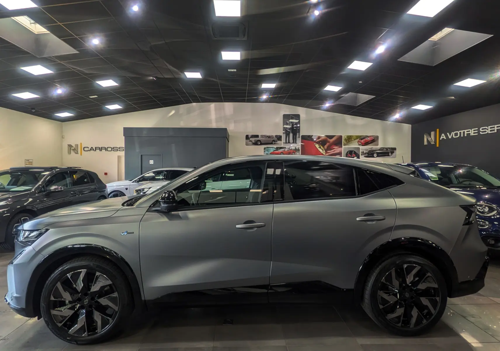 Profil côté gauche du Renault Rafale E-TECH gris schiste satin, SUV hybride 2025 en showroom avec jantes noires distinctives.