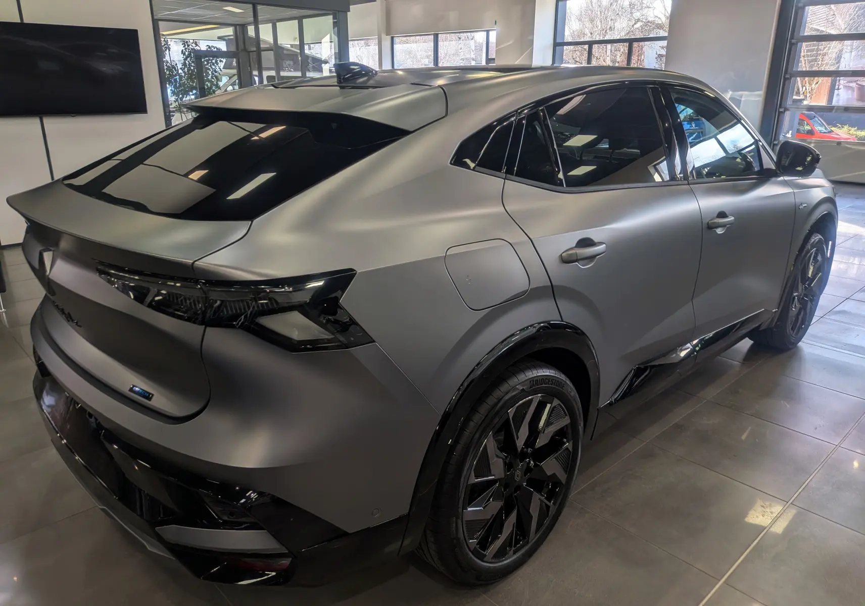 Vue 3/4 arrière droite d’une Renault Rafale E-TECH gris schiste satin avec jantes noires et vitres teintées en showroom.