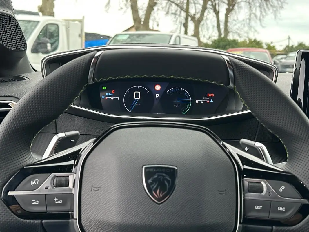 Vue intérieure centrée sur le volant Peugeot 208 Hybrid 110 e-DCS6 GT avec cockpit numérique et coutures vertes.
