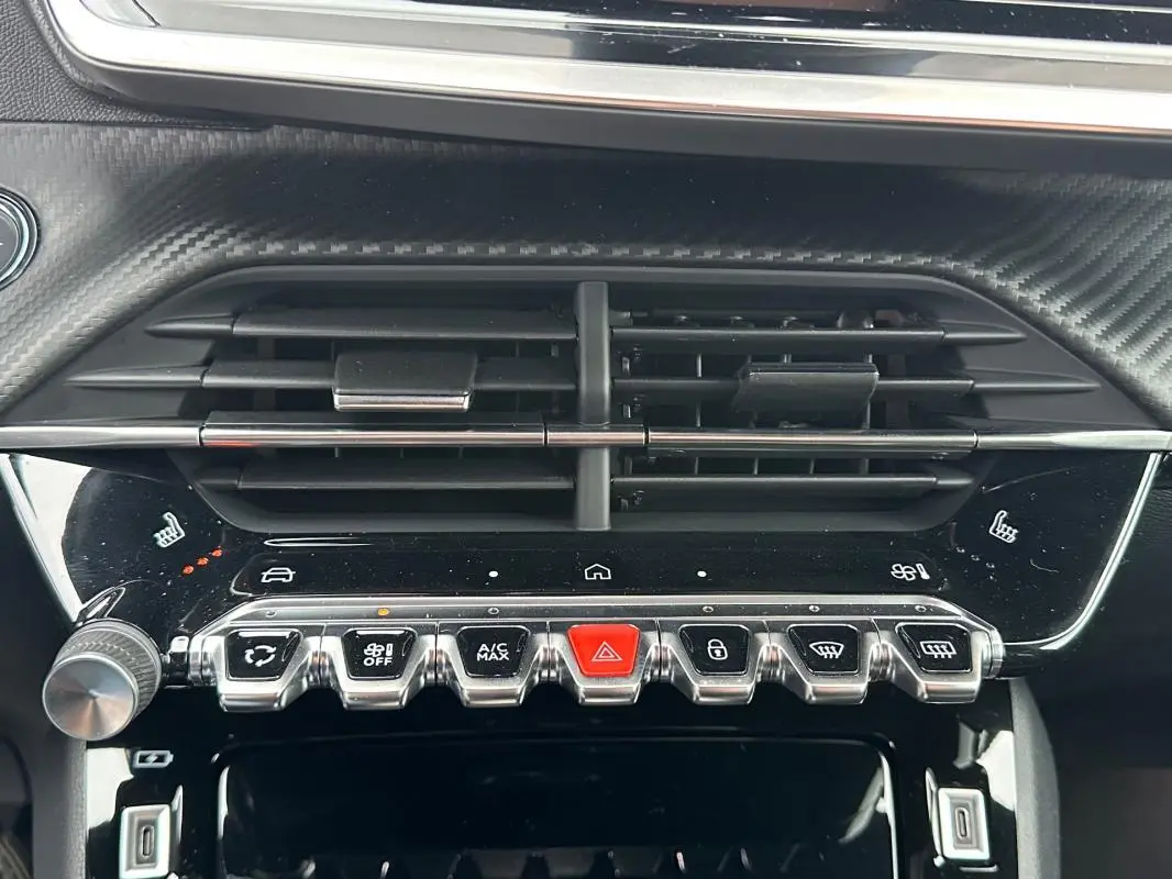 Détail du tableau de bord de la Peugeot 208 Hybrid 110 GT montrant les commandes de climatisation et les aérateurs noirs.