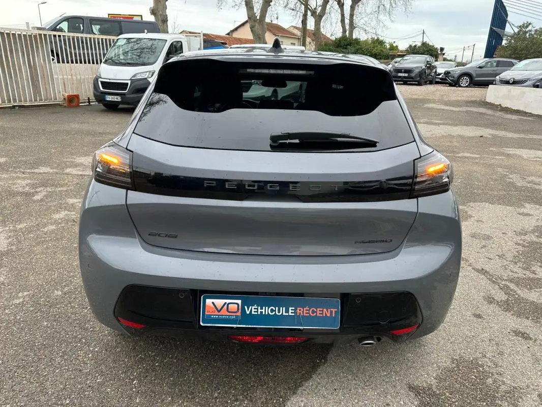 Vue arrière d'une Peugeot 208 gris 2025 avec feux arrière allumés et logo Peugeot en noir brillant.