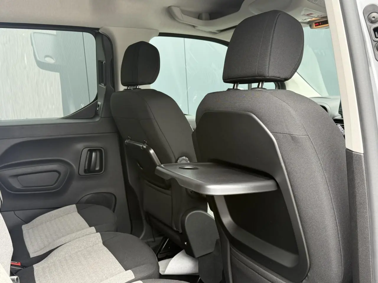 Vue intérieure arrière droite du Citroën Berlingo Multispace gris acier, montrant les sièges avec tablette rabattable intégrée.