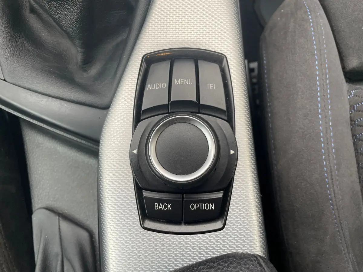 Gros plan sur la molette de commande iDrive noire et argentée au centre de la console d'une BMW Série 2 Coupé blanche.