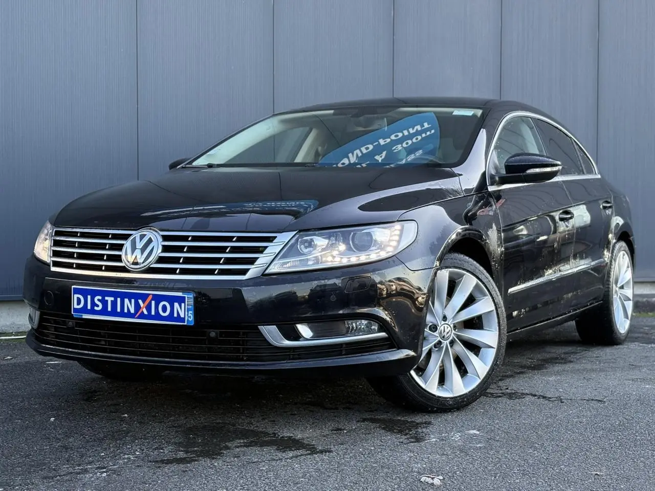 Volkswagen Passat CC 1.4 TSI 2015 en Deep Black, vue 3/4 avant avec jantes alliage 18 pouces et phares allumés.