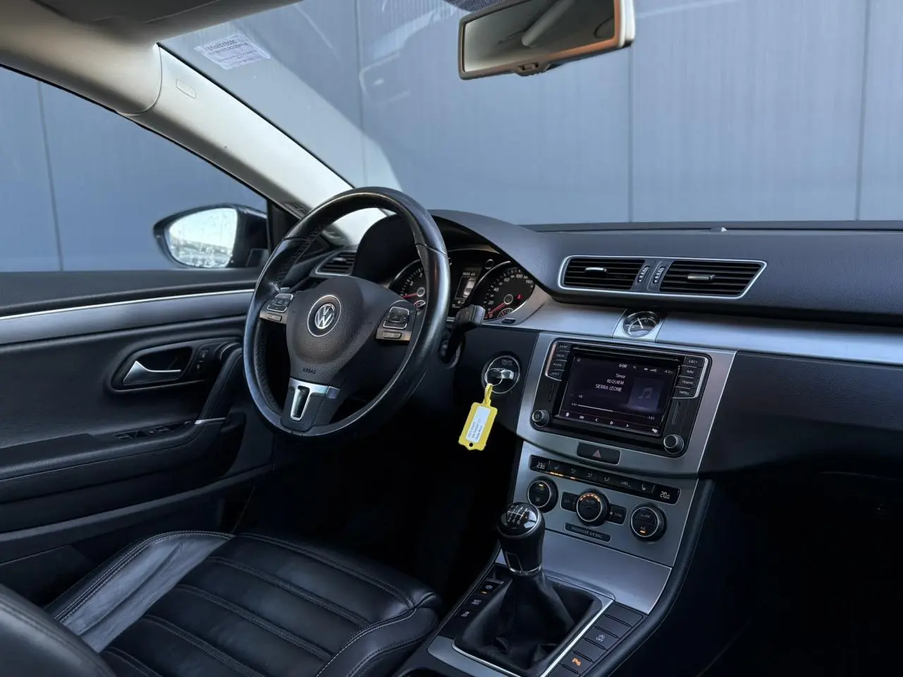 Vue intérieure côté conducteur de la Volkswagen Passat CC 1.4 TSI 2015 avec sellerie cuir noire et tableau de bord moderne.