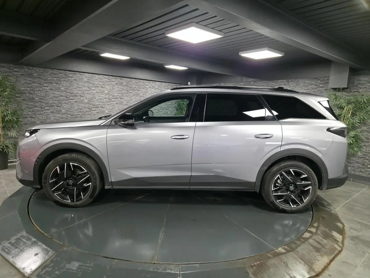 Vue de profil côté gauche d’un Peugeot 5008 gris métallisé avec jantes alliage noires dans un showroom.