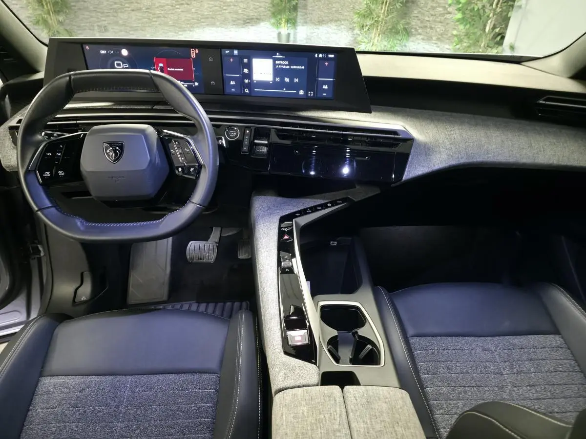 Vue intérieure avant du Peugeot 5008 2025 hybride, tableau de bord avec double écran et volant compact cuir noir.