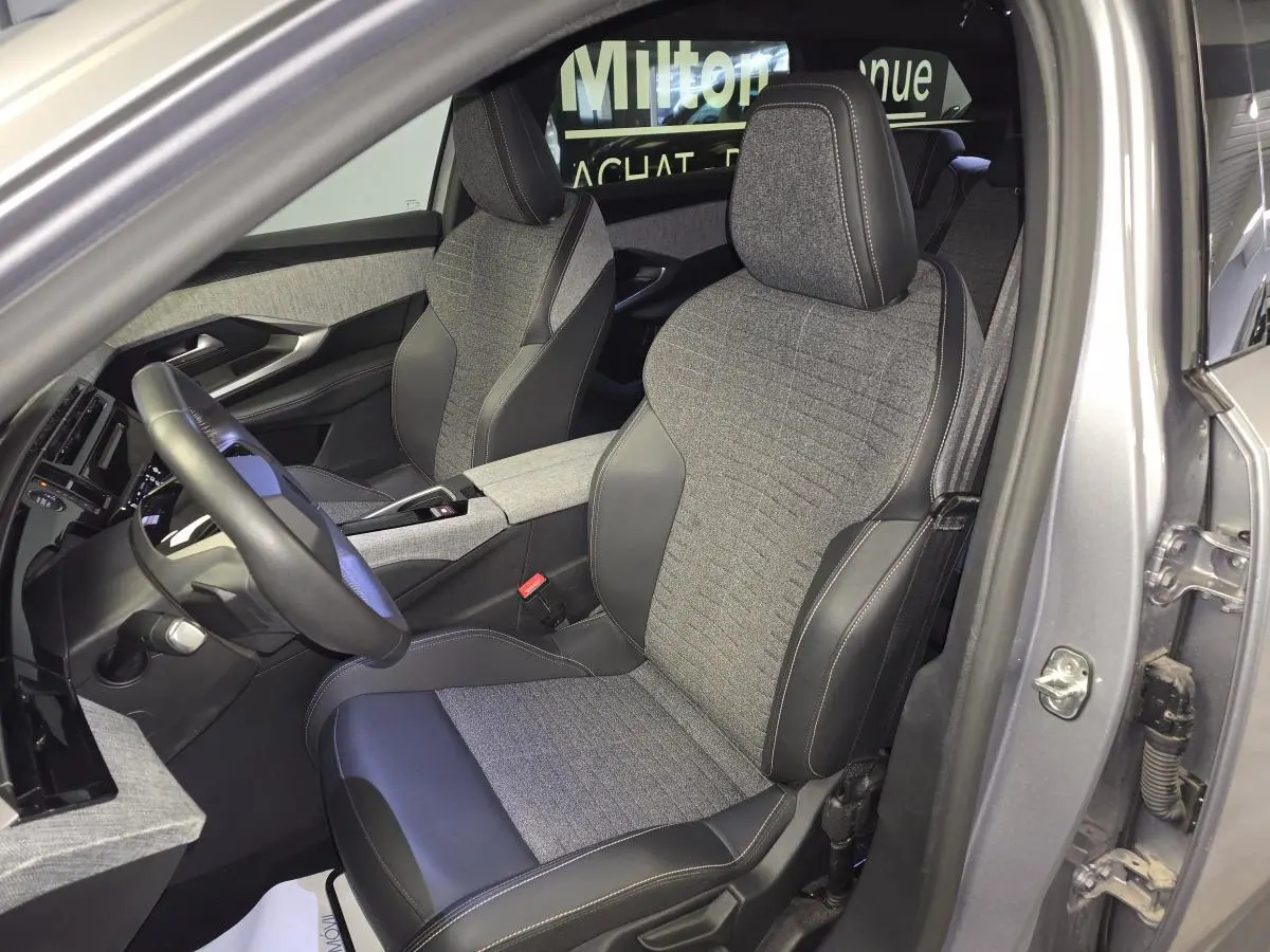 Vue intérieure côté conducteur du Peugeot 5008 gris 2025, mettant en valeur les sièges tissu et cuir avec surpiqûres contrastées.