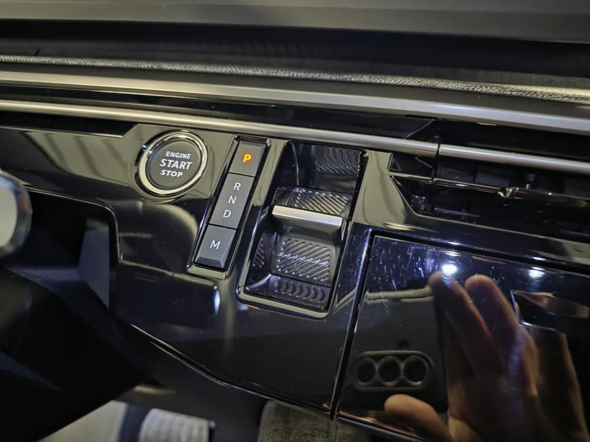 Gros plan sur la console centrale noire laquée du Peugeot 5008 hybride 2025 avec bouton start/stop et sélecteur de boîte automatique.