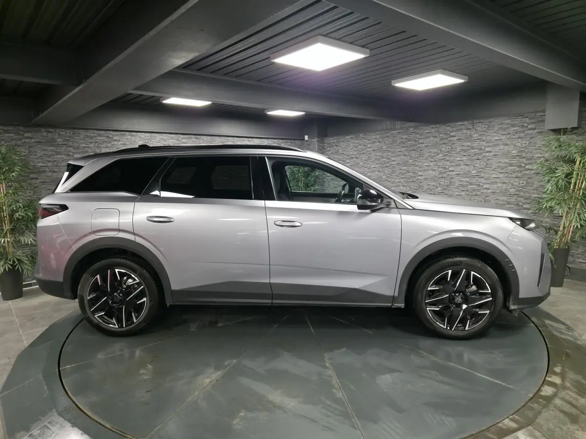Vue de profil côté gauche d'un Peugeot 5008 gris métallisé avec jantes alliage noires diamantées dans un showroom.