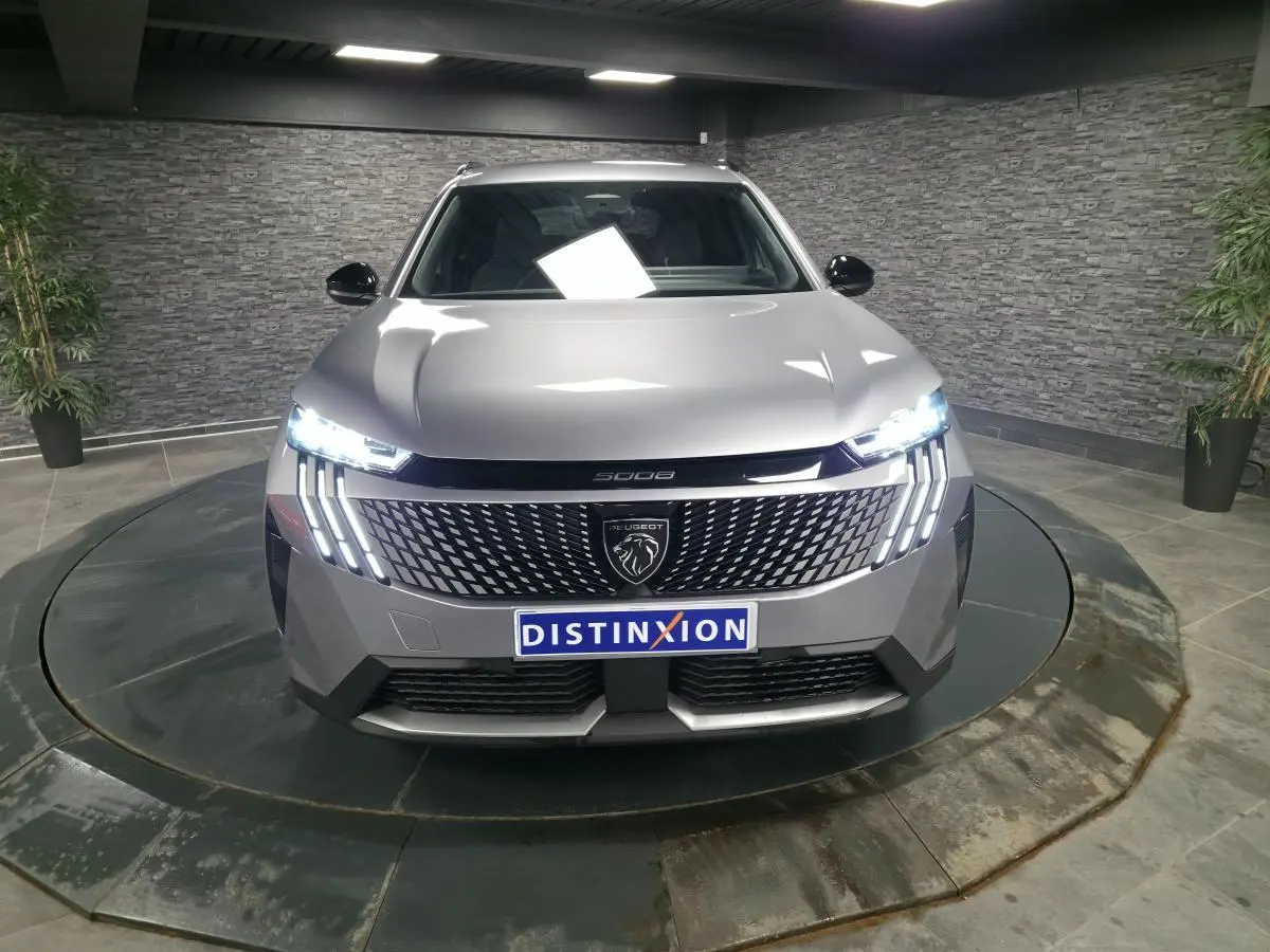Vue frontale d'un Peugeot 5008 gris métallisé 2025 avec feux LED allumés et calandre au lion distinctif.