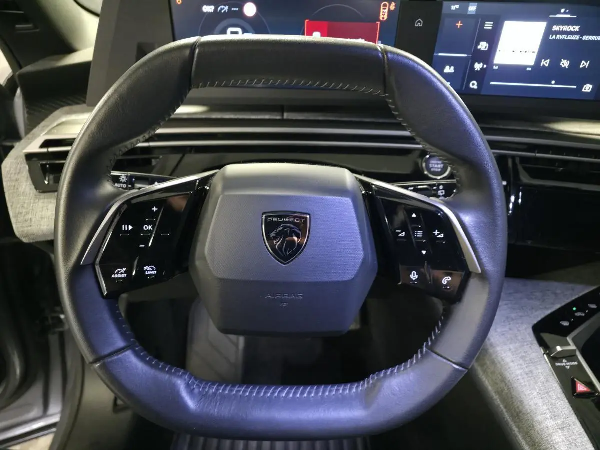 Volant cuir noir au design compact avec logo Peugeot, vue frontale de l'habitacle du 5008 hybride gris 2025.