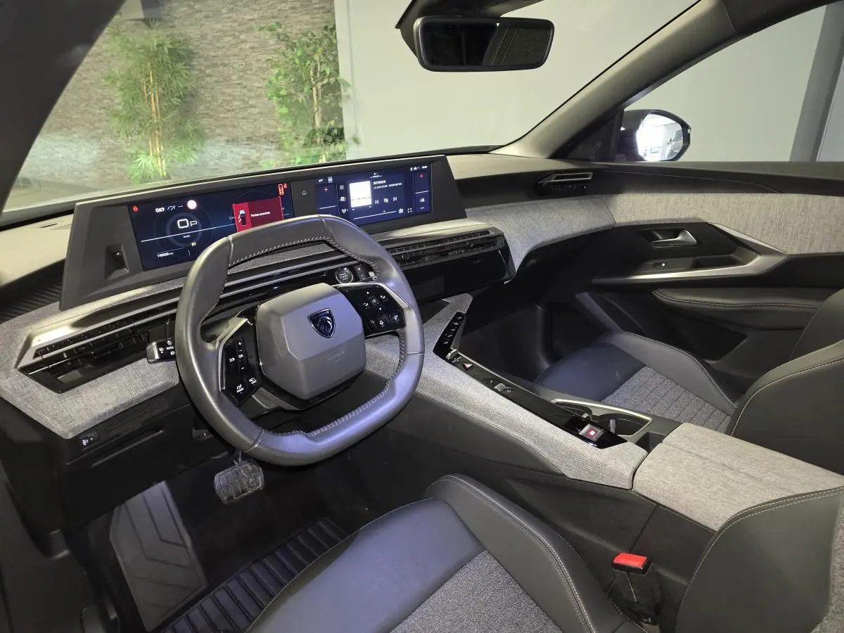 Vue intérieure côté conducteur du Peugeot 5008 gris 2025, avec tableau de bord numérique panoramique et volant compact cuir noir.
