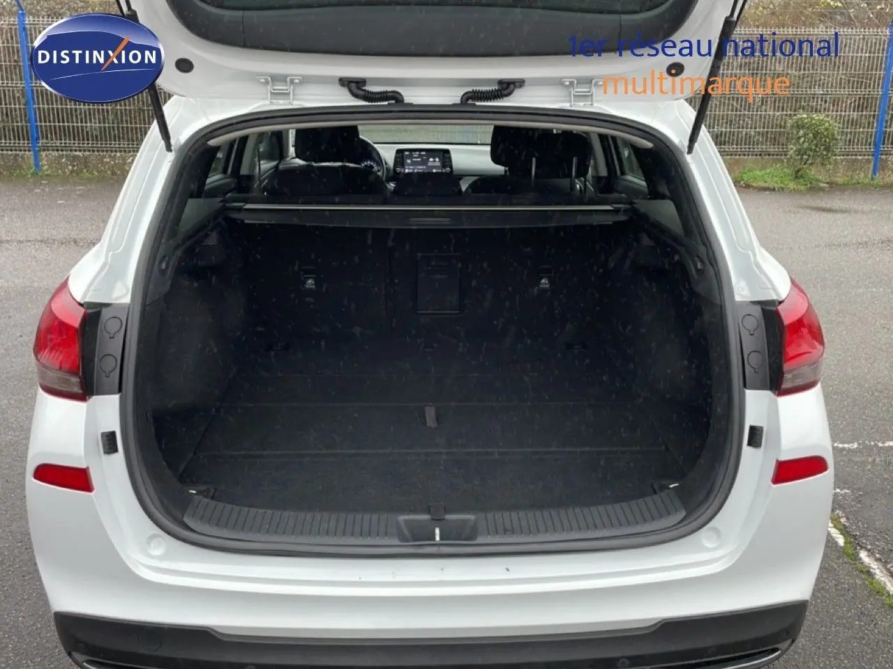 Vue arrière ouverte sur le coffre spacieux d’une Hyundai i30 SW blanche polaire, avec intérieur sombre visible.