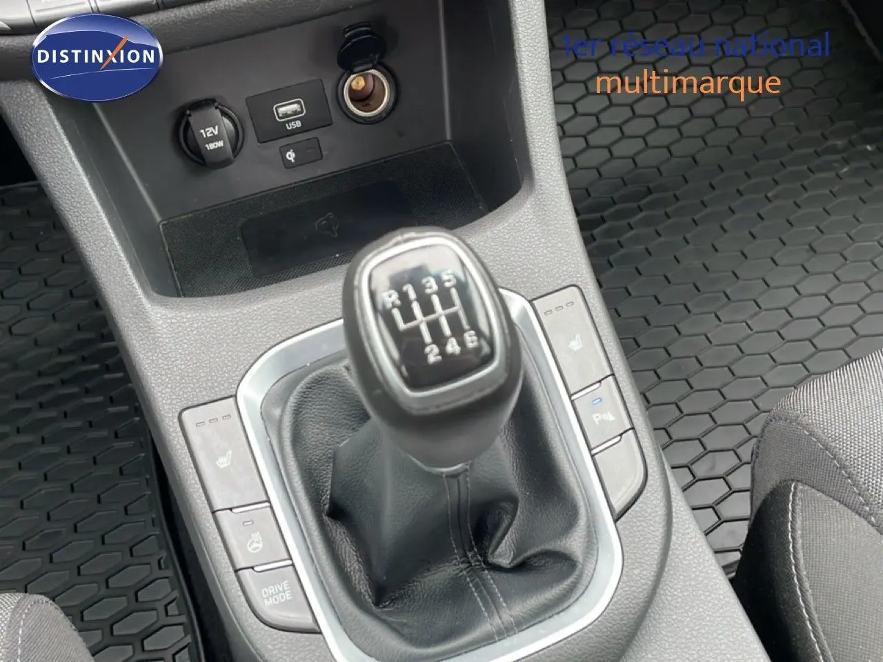 Gros plan sur le levier de vitesses manuel de la Hyundai i30 SW blanche, entouré de commandes et tapis caoutchouc noir.
