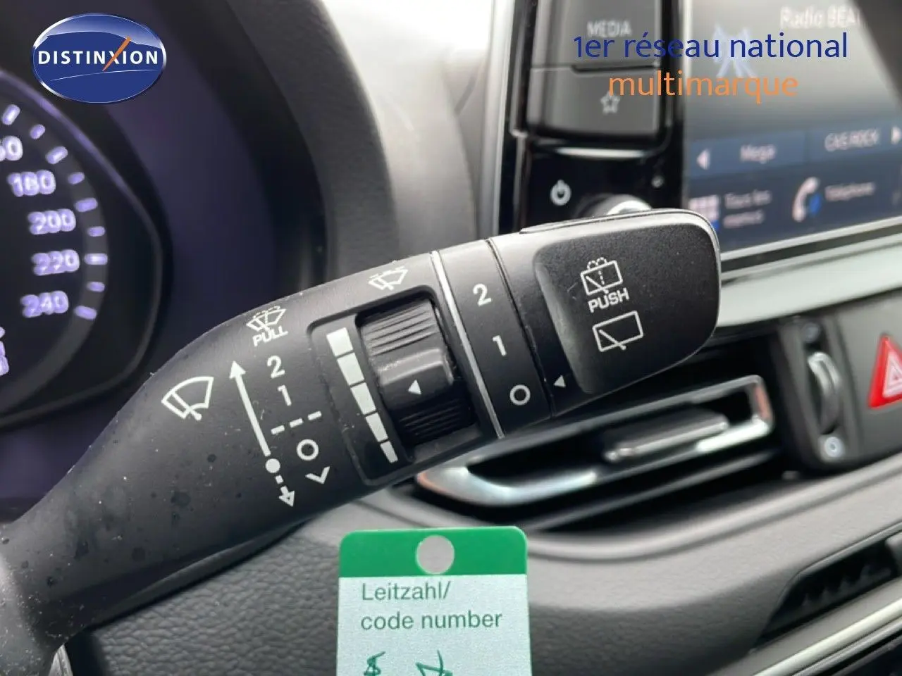 Gros plan sur la manette d’essuie-glace du tableau de bord d’une Hyundai i30 SW blanc polaire, avec affichage digital en arrière-plan.