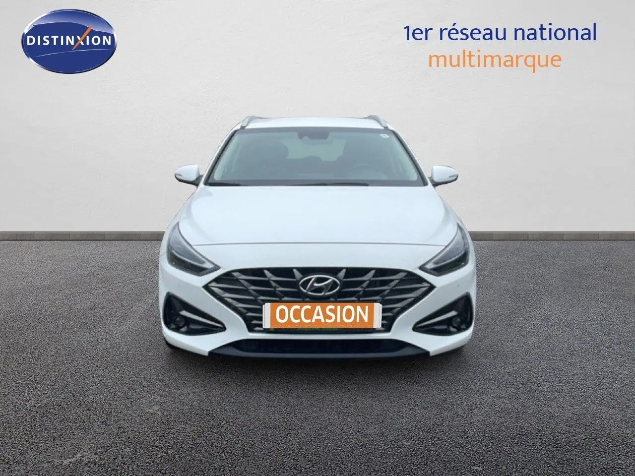 Vue frontale d'une Hyundai i30 SW blanche polaire, avec calandre noire et phares LED allumés.