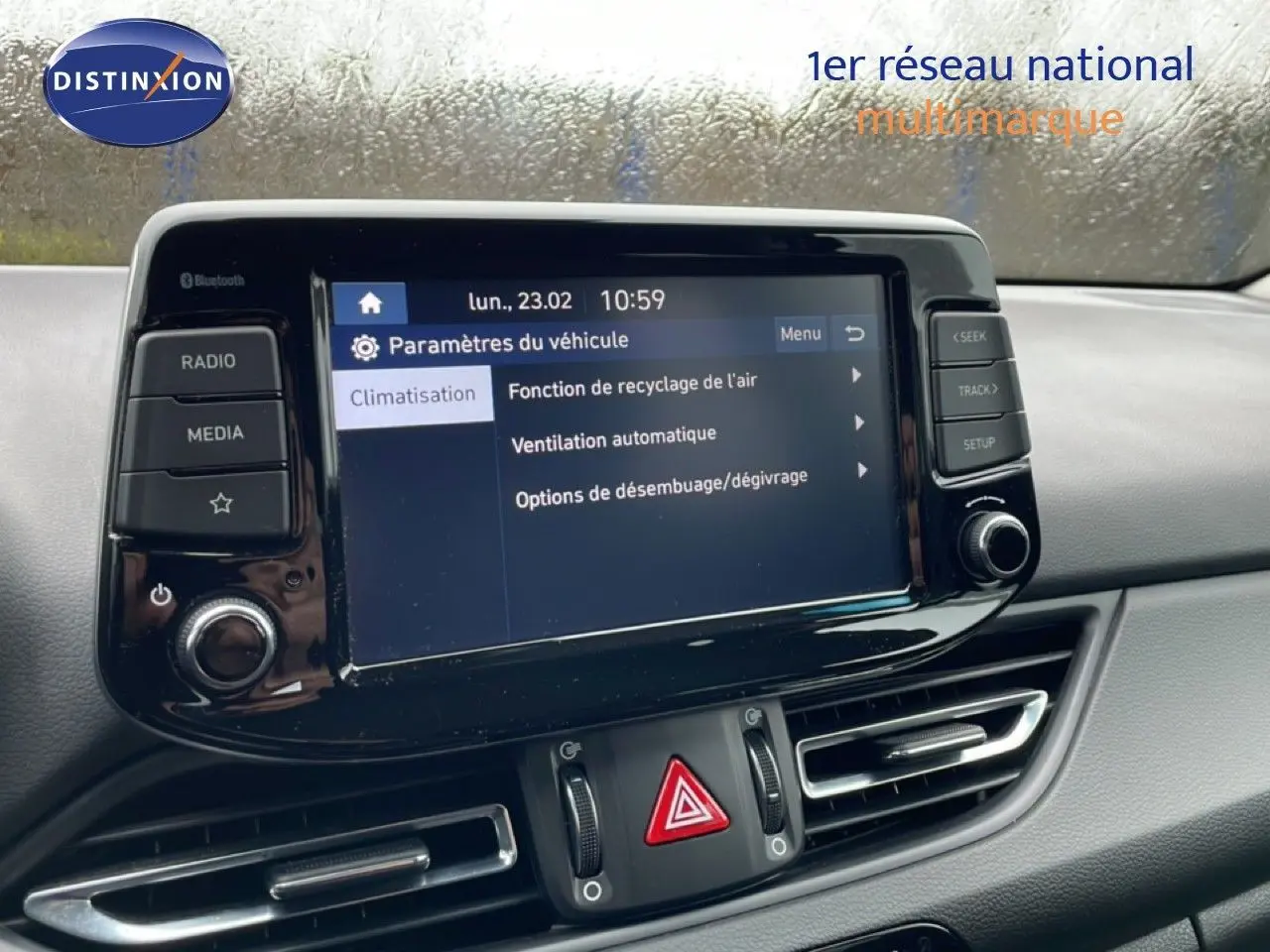 Vue intérieure centrée sur l'écran tactile du tableau de bord de la Hyundai i30 SW blanc polaire, avec commandes climatisation visibles.