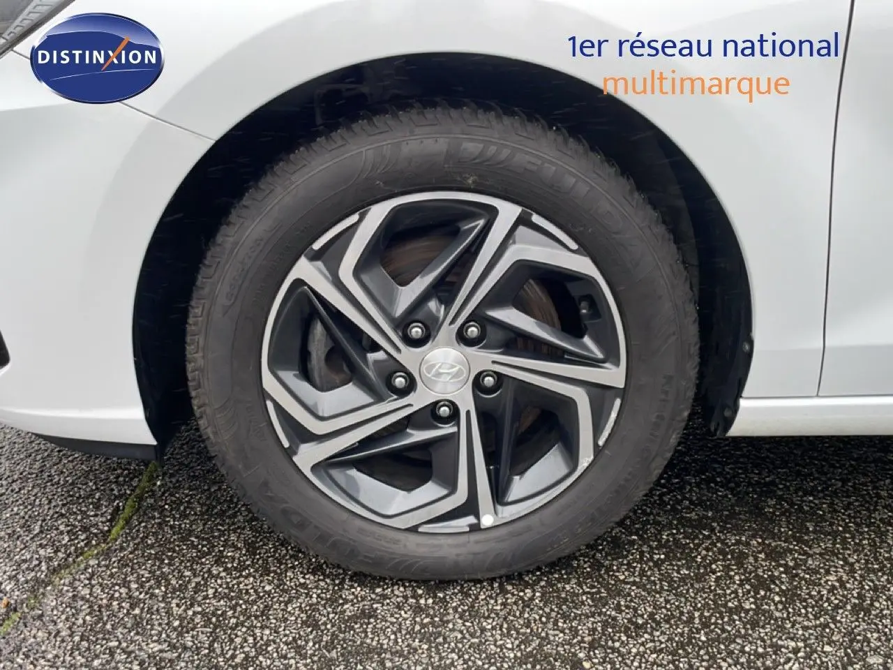 Gros plan sur la roue avant gauche d'une Hyundai i30 SW blanche polaire, mettant en valeur la jante alliage au design moderne.