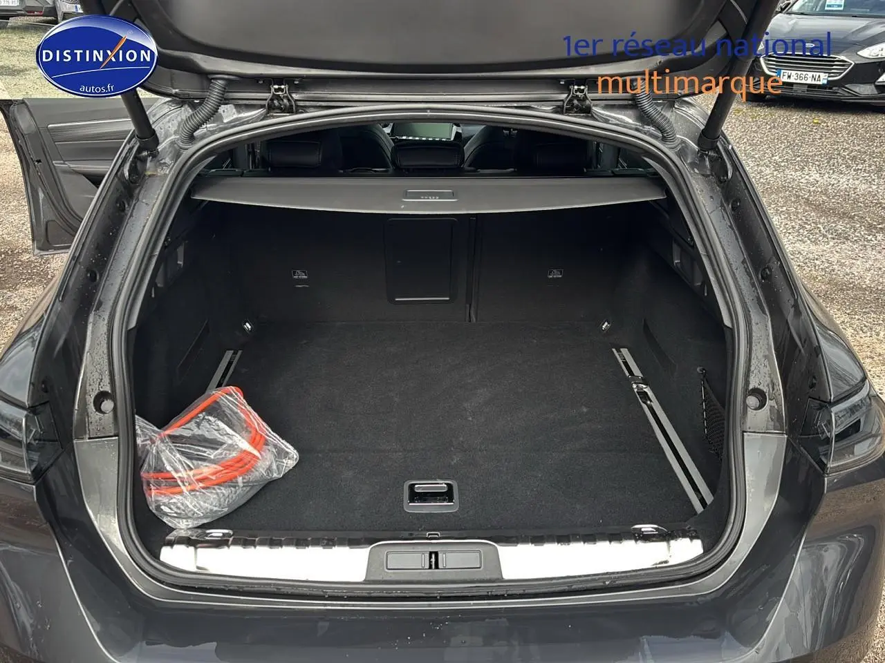 Coffre ouvert vu de l'arrière d'une Peugeot 508 SW Hybrid 225 gt e-eat8 gris titane avec tapis noir et accessoires emballés.