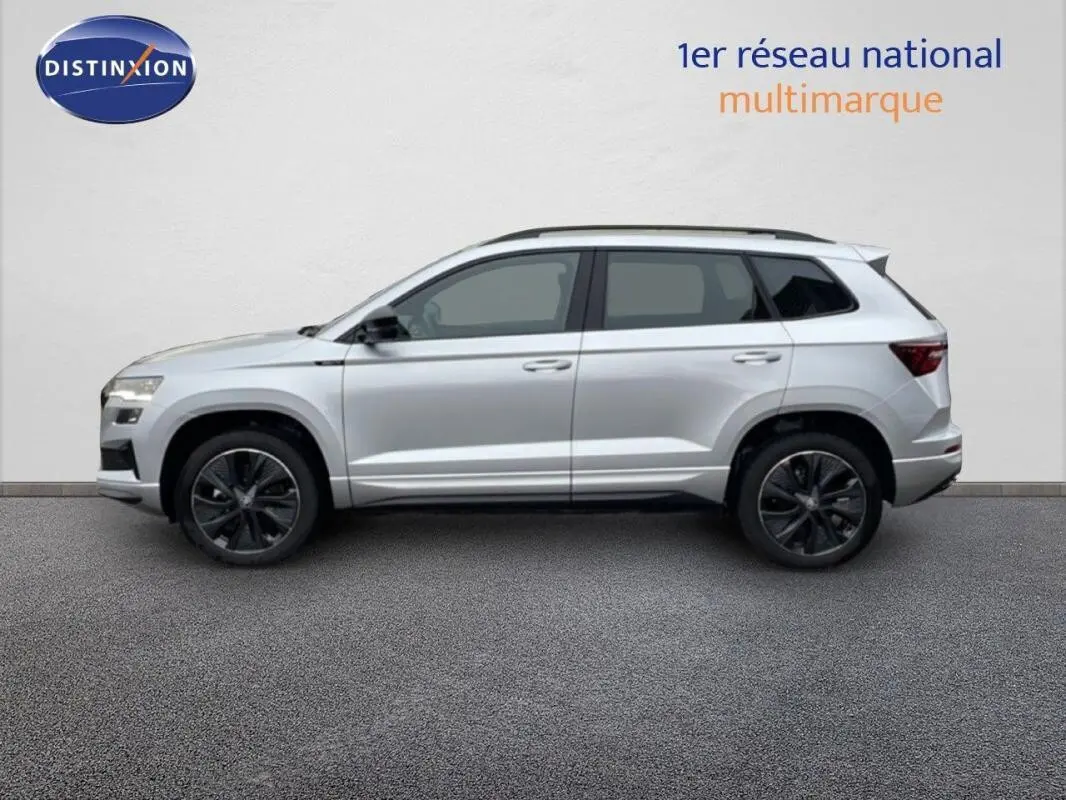 Vue latérale droite d'un Skoda Karoq argent 2025 avec barres de toit et jantes noires sportline.