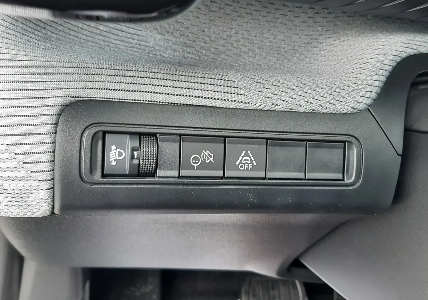Gros plan sur les commandes d'assistance et réglage des phares du Citroën C3 Aircross 1.2 Hybrid 145 gris Mercury, intérieur côté conducteur.