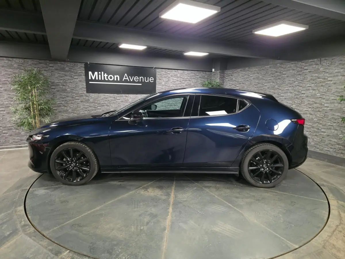 Vue latérale droite d'une Mazda3 2024 bleu métallisé avec jantes alliage noires dans un showroom intérieur.