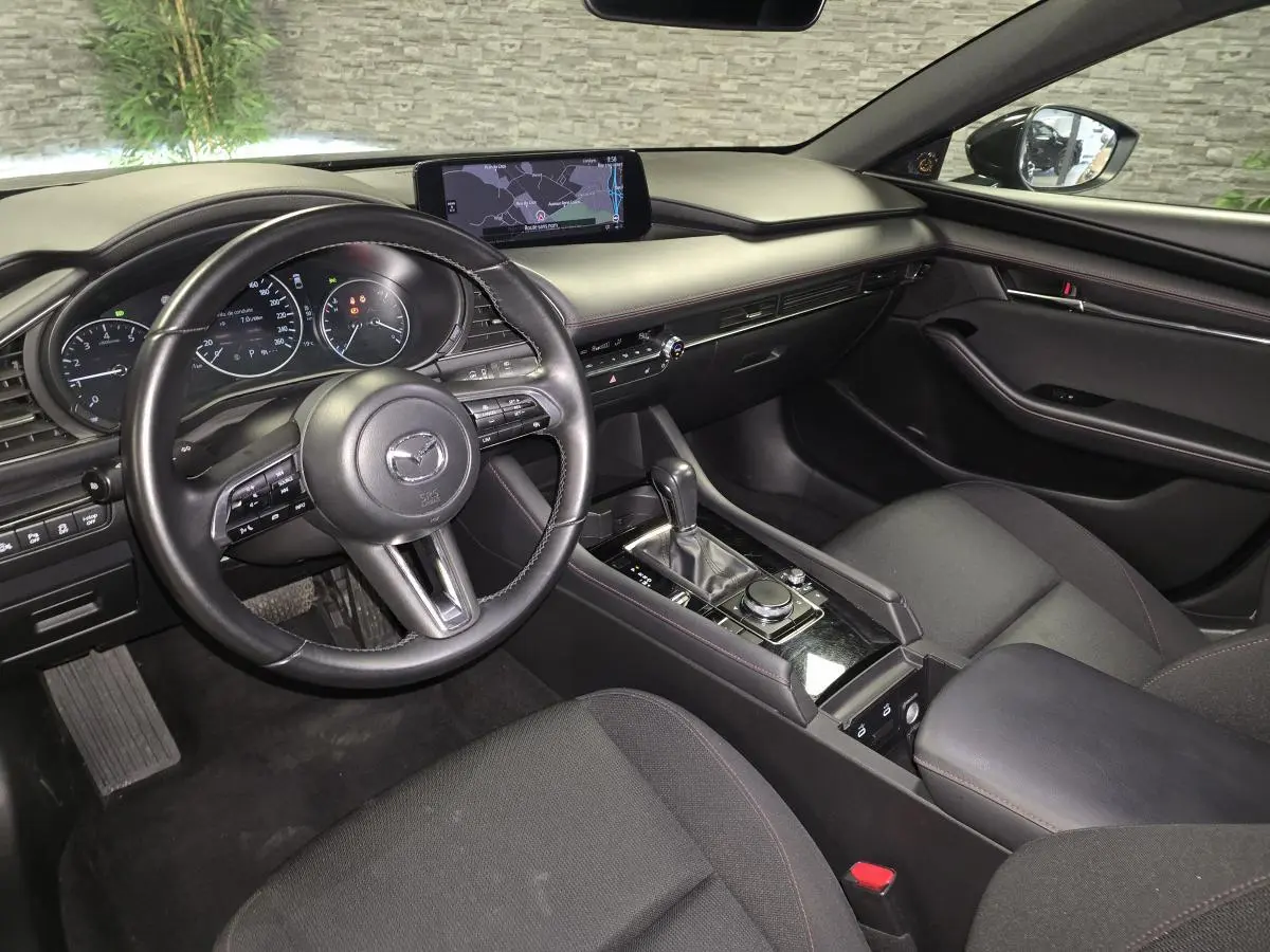 Intérieur noir de la Mazda3 2024 vu côté conducteur, avec tableau de bord moderne et écran central tactile.