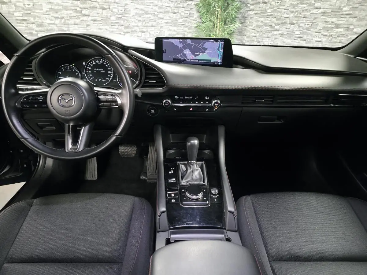 Vue intérieure avant de la Mazda3 2024, tableau de bord noir avec écran central et volant cuir multifonction.