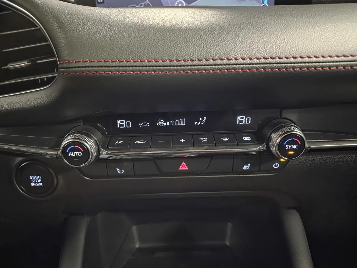 Gros plan sur la console centrale noire de la Mazda3 2024, affichant la climatisation automatique et le bouton start/stop.